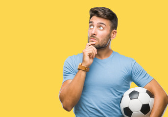 Young handsome man holding soccer football ball over isolated background serious face thinking...