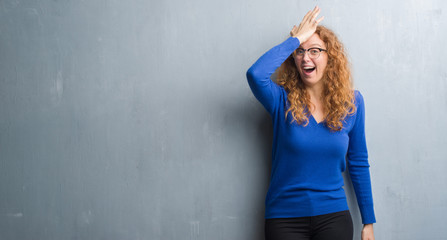 Young redhead woman over grey grunge wall surprised with hand on head for mistake, remember error....