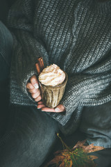Woman in dark woolen sweater and grey jeans sitting and holding mug with hot chocolate or coffee...