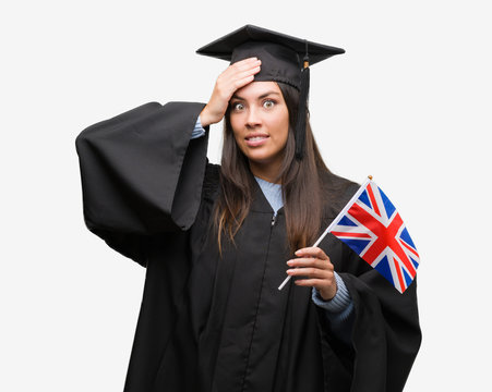 Young hispanic woman wearing graduated uniform holding flag of united kingdom stressed with hand on head, shocked with shame and surprise face, angry and frustrated. Fear and upset for mistake.