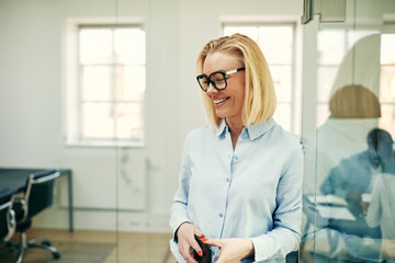 Laughing businesswoman holding a cellphone in a modern office