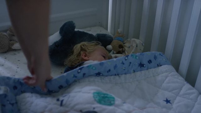 Mother covering her toddler asleep in their cot for an afternoon nap