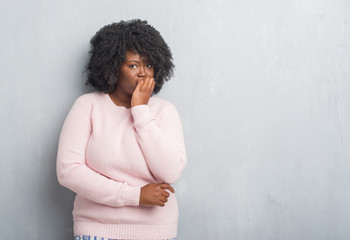 Young african american plus size woman over grey grunge wall wearing winter sweater looking stressed and nervous with hands on mouth biting nails. Anxiety problem.