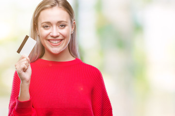 Young blonde woman holding credit card over isolated background with a happy face standing and smiling with a confident smile showing teeth