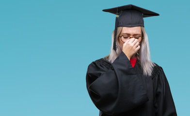 Young blonde woman wearing graduate uniform over isolated background tired rubbing nose and eyes feeling fatigue and headache. Stress and frustration concept.