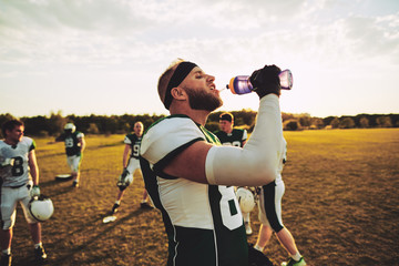 American football player drinking water during practice outside