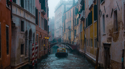 Fototapeta na wymiar Single boat cruising on a canal in Venice Italy, winter foggy morning