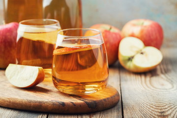 Organic Apple cider or juice on a wooden table. Two glasses with drink and autumn leaves on rustic background