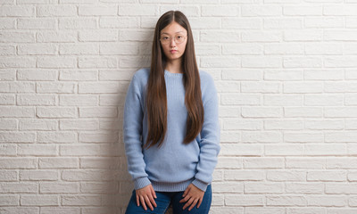 Young Chinise woman over white brick wall with serious expression on face. Simple and natural looking at the camera.