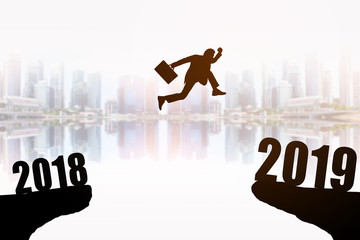 Silhouette of young businessman jumping between 2018 and 2019 years with beautiful the skyscrapers background, concepts of news year and business target.
