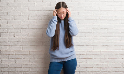 Young Chinise woman over white brick wall with hand on head for pain in head because stress. Suffering migraine.