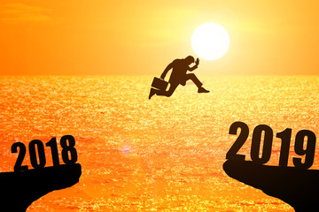 Silhouette of young businessman jumping between 2018 and 2019 years with beautiful sunset at the sea, concepts of news year and business target.