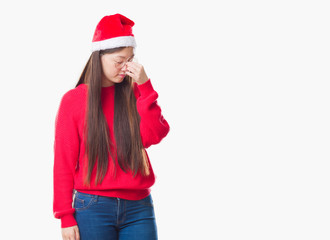 Young Chinese woman over isolated background wearing christmas hat tired rubbing nose and eyes feeling fatigue and headache. Stress and frustration concept.