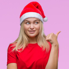 Young caucasian woman wearing christmas hat over isolated background smiling with happy face looking and pointing to the side with thumb up.