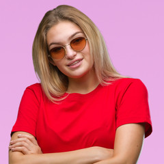 Young caucasian woman wearing sunglasses over isolated background happy face smiling with crossed arms looking at the camera. Positive person.