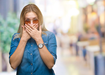 Young caucasian woman wearing sunglasses over isolated background shocked covering mouth with hands for mistake. Secret concept.