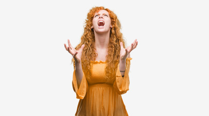 Young redhead woman crazy and mad shouting and yelling with aggressive expression and arms raised. Frustration concept.