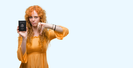 Young redhead woman holding passport of United States of America with angry face, negative sign showing dislike with thumbs down, rejection concept