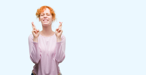 Young redhead woman smiling crossing fingers with hope and eyes closed. Luck and superstitious concept.