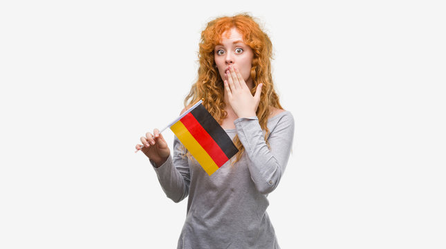 Young redhead woman holding flag of Germany cover mouth with hand shocked with shame for mistake, expression of fear, scared in silence, secret concept