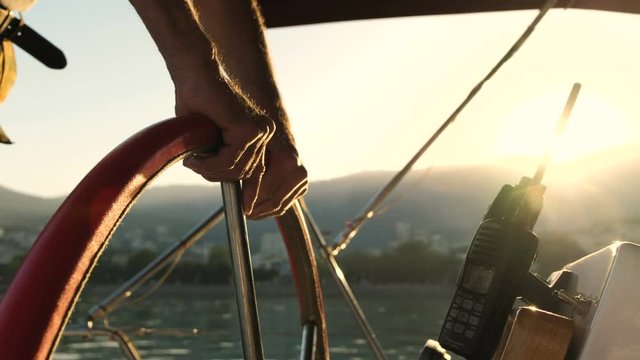Close up Captains hands driving his boat at sunset.