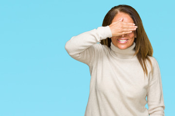 Naklejka premium Beautiful middle age adult woman wearing winter sweater over isolated background smiling and laughing with hand on face covering eyes for surprise. Blind concept.