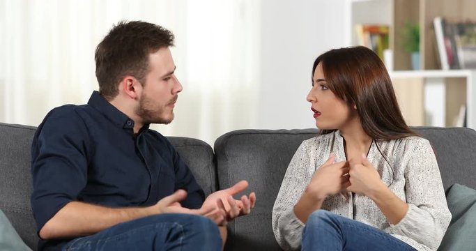 Angry couple arguing sitting on a couch in the living room at home