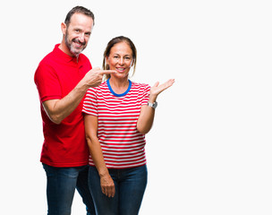 Middle age hispanic couple in love over isolated background amazed and smiling to the camera while presenting with hand and pointing with finger.