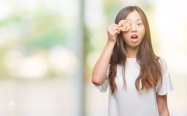 Fototapeta premium Young asian woman eating chocolate chip cookie over isolated background scared in shock with a surprise face, afraid and excited with fear expression