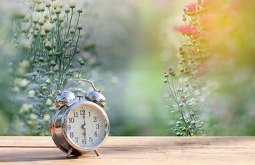 Naklejka premium Vintage alarm clock on wooden table with green nature bokeh background.with copy space for text.