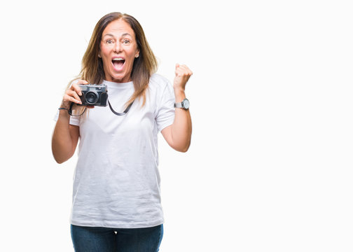 Middle age hispanic woman taking pictures using vintage photo camera over isolated background screaming proud and celebrating victory and success very excited, cheering emotion