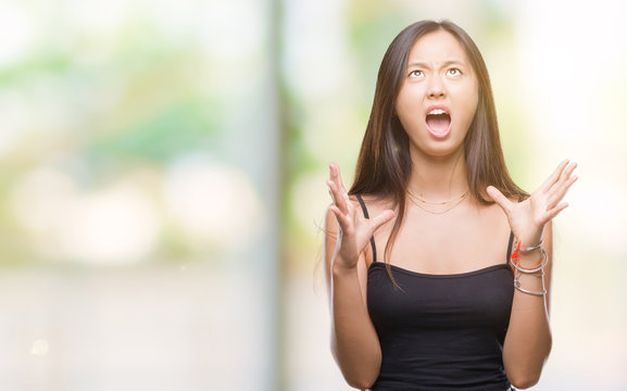 Young asian woman over isolated background crazy and mad shouting and yelling with aggressive expression and arms raised. Frustration concept.