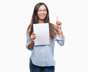 Young asian woman holding blank paper over isolated background surprised with an idea or question pointing finger with happy face, number one