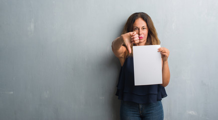 Middle age hispanic woman holding bank paper sheet with angry face, negative sign showing dislike with thumbs down, rejection concept