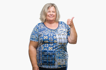 Senior plus size caucasian woman over isolated background smiling with happy face looking and pointing to the side with thumb up.