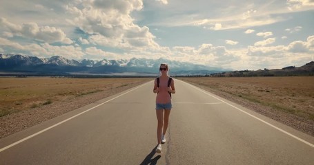 Young woman backpacker walking on road. Mountains at background.