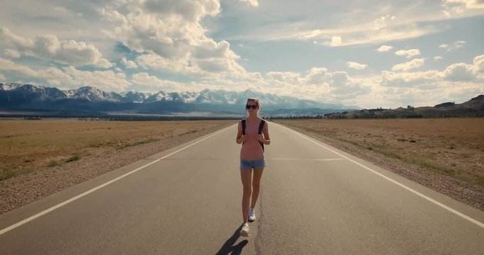 Young woman backpacker walking on road. Mountains at background.