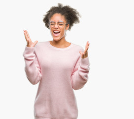 Young afro american woman wearing glasses over isolated background celebrating mad and crazy for success with arms raised and closed eyes screaming excited. Winner concept