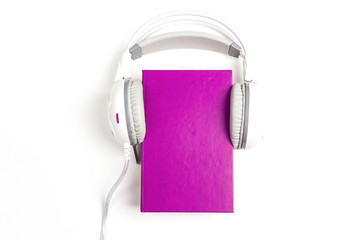 Purple book with a white  headphones on it on white background. Audio book concept.