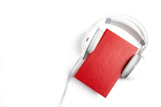 Red book with a white  headphones on it on white background. Audio book concept.