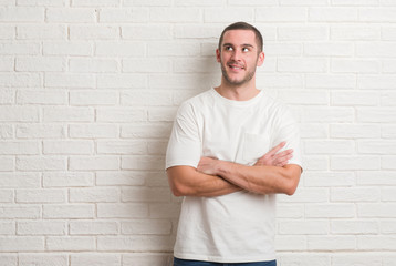 Young caucasian man standing over white brick wall smiling looking side and staring away thinking.