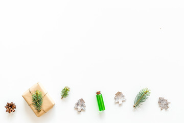 Composition with New Year gift wrapped in craft paper and decorted with pine sprout near pine sprigs, cones, spruce figure, fir oil on white background top view copy space