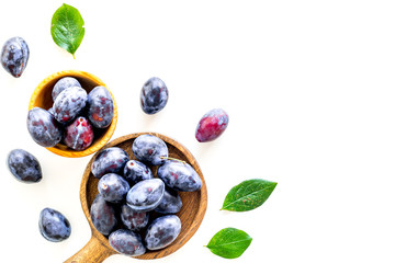 Plums on dinning table. Fresh raw purple plum in wooden bowl on white background top view space for...