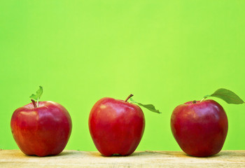 Red apples on wooden table in front of green background.