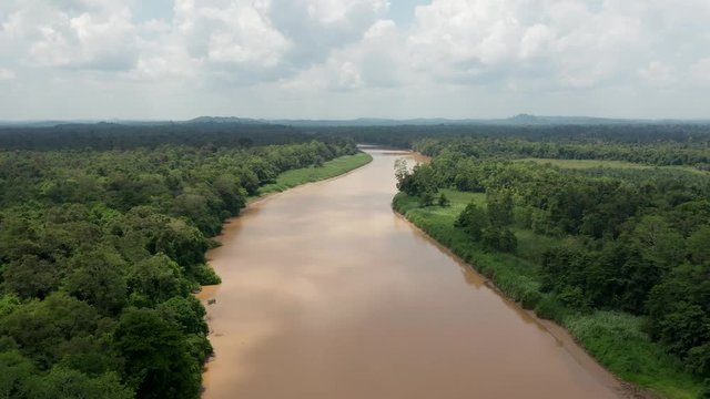 Aerial drone view flying backwards over a large, brown river running through tropical rainforest (Kinabatangan, Borneo)