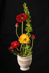 Floral arrangement from artificial poppy flowers in old ceramic flower pot.