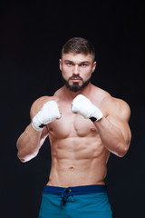 Muscular Fighter kickbox With white Bandages against the black background.