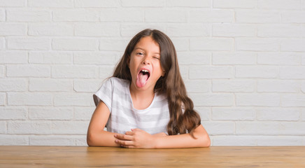 Young hispanic kid sitting on the table at home sticking tongue out happy with funny expression. Emotion concept. © Krakenimages.com