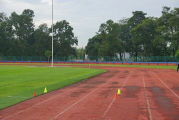 track and fields with 2 yellow cone on track with artificial grass inside a stadium