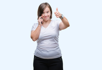 Young adult woman with down syndrome taking using smartphone over isolated background happy with big smile doing ok sign, thumb up with fingers, excellent sign
